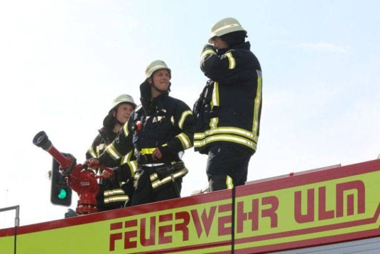 Drei Angehörige der Freiwilligen Feuerwehr Ulm stehen auf dem Dach des Großtanklöschfahrzeuges und bedienen den Wasserwerfer bei einem Brand.