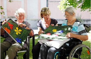 Freiwillige mit 2 Seniorinnen und deren selbst gemalten Bildern